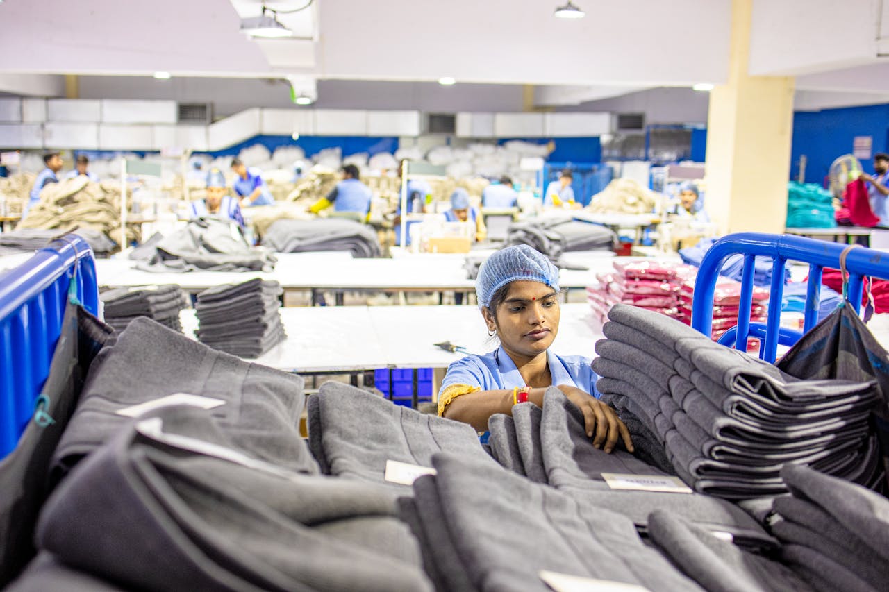 hero-img-01 Textile worker sorting fabric piles in a busy South Asian apparel factory.