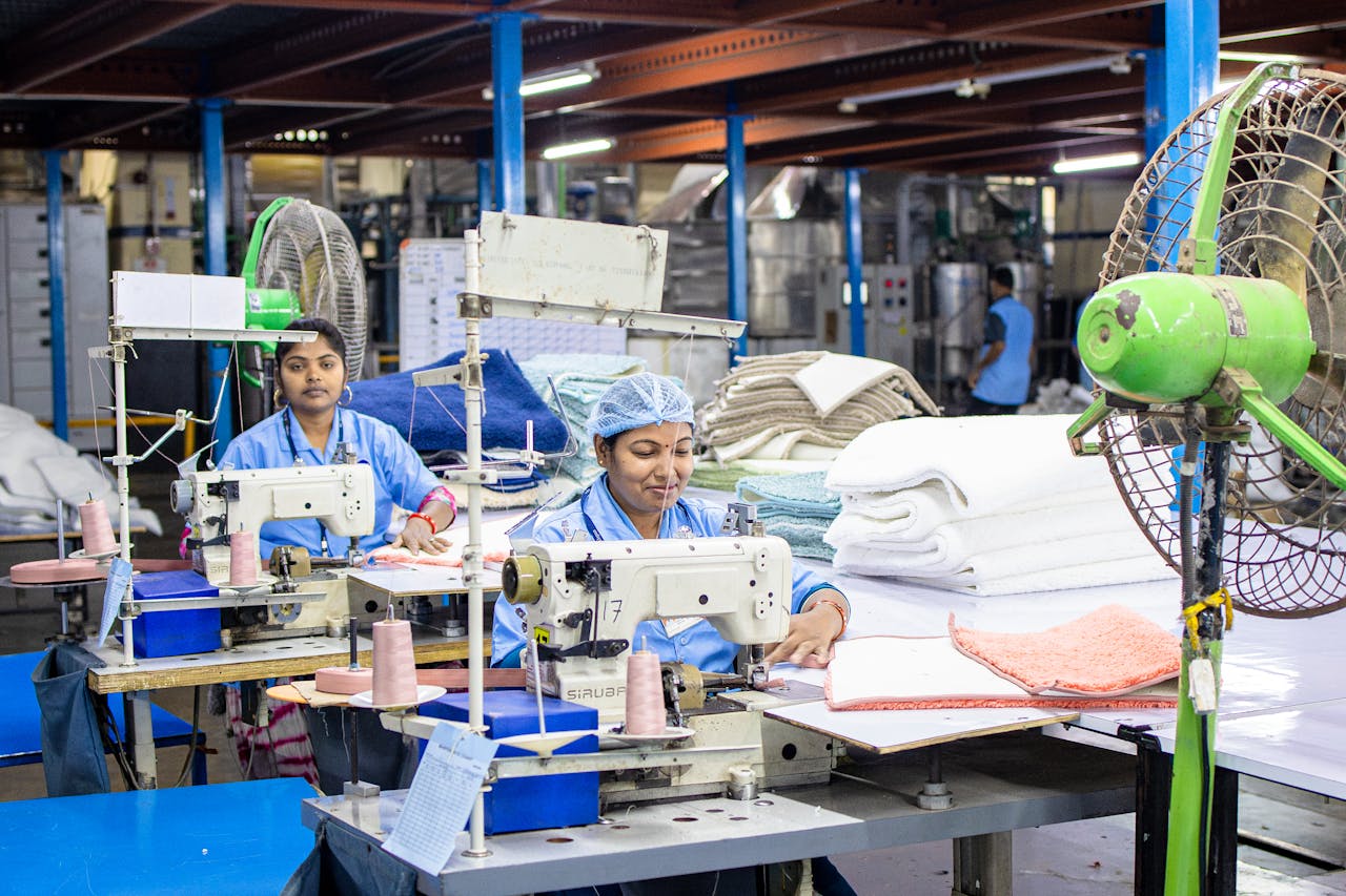 hero-img-02 Female workers sew textiles in an Indian factory, showcasing industrial textile production.